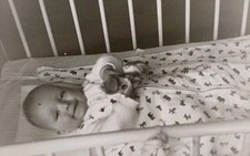 Lachendes Baby liegt im Schlafsack mit Rassel im Gitterbett Kleinkind Altes Foto