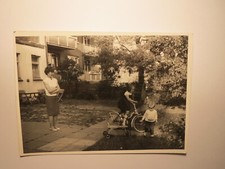 Kleines Mädchen mit Fahrrad & Kleinkind mit Dreirad ? - Frau im Garten / Foto