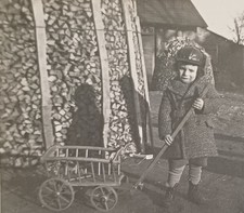 Kleiner Junge im Mantel mit Mütze und Bollerwagen vor Holzstapel Bauernhof Foto