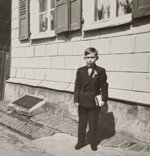 Junge steht stolz im Anzug mit Buch vor Haus Kommunion Konfirmation Foto
