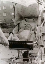 Süßes schlafendes Baby im Kinderwagen vor Plattenbau Neubaublock Altes Foto