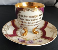 Antike Porzellantasse und Untertasse mit Spruch auf drei Füßen