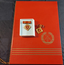 2 DDR Aktivistenabzeichen mit Spange und Urkundenmappe