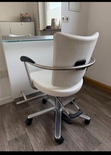 Ein Friseurstuhl, ein Spiegel mit Ablage und Föhnhalter und ein Waschbecken