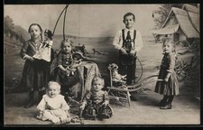 Foto-AK Kindergruppe mit Puppen u. Schubkarre vor Fotokulisse 