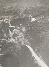 Junge Frau sitzt waghalsig oberhalb eines Wasserfalls in 20er Jahre Kleid Foto