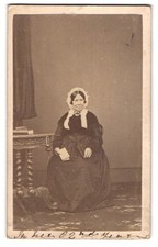 Fotografie 82 jährige Dame im dunklen Biedermeierkleid mit Haube sitzend im Ate 