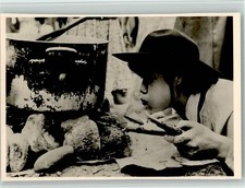 40136431 - Kochtopf steht auf Feuersteinen und Junge blaest die Glut an Kind